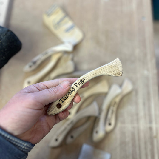 Hand holding a wooden Hera Marker with 'Thread Pegs' branding against a wooden background.