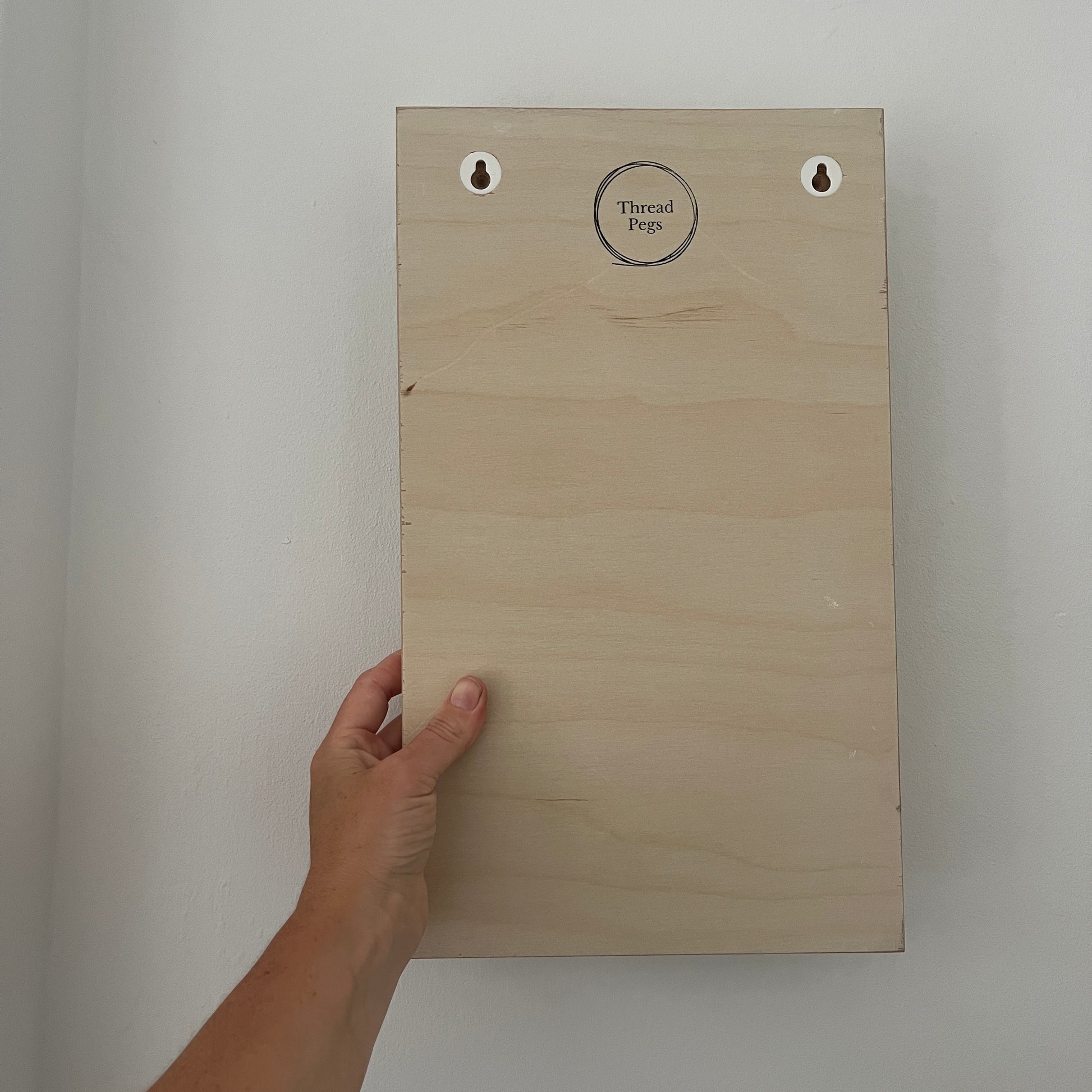 Wooden peg board held by a hand against a plain background
