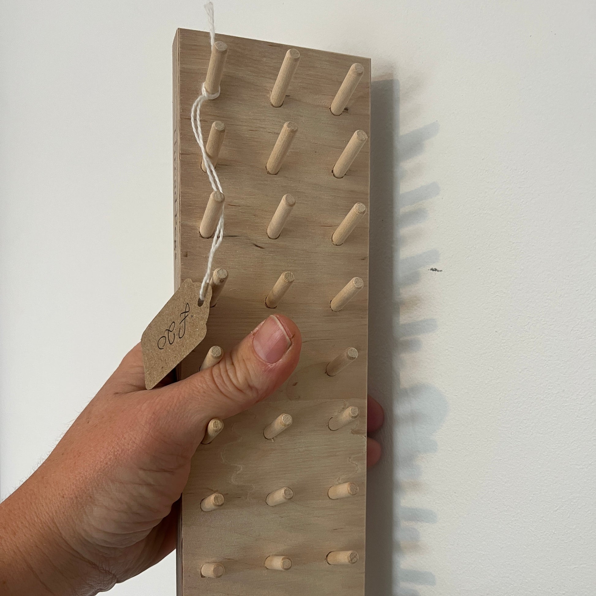 Hand holding a wooden pegboard against a white background