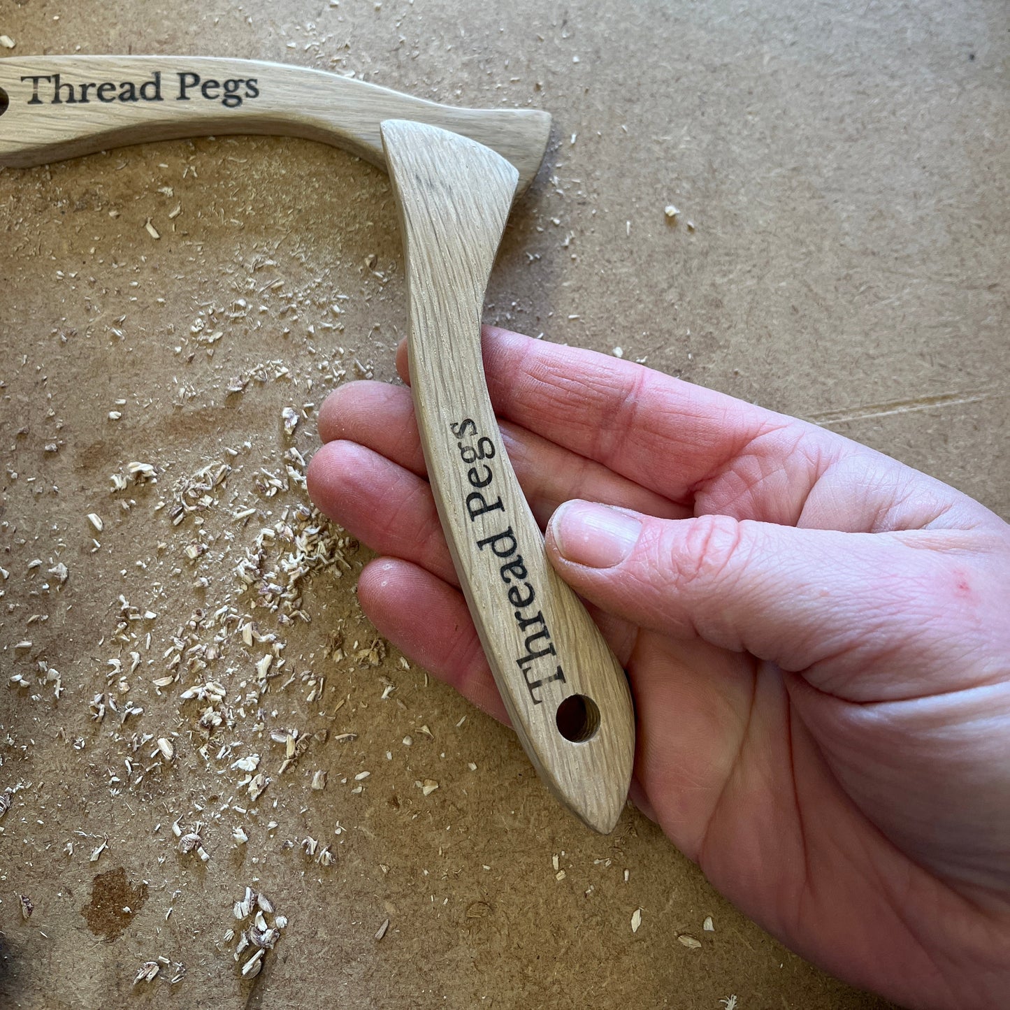 Hand holding a wooden tool with 'Thread Pegs' branding on a beige background