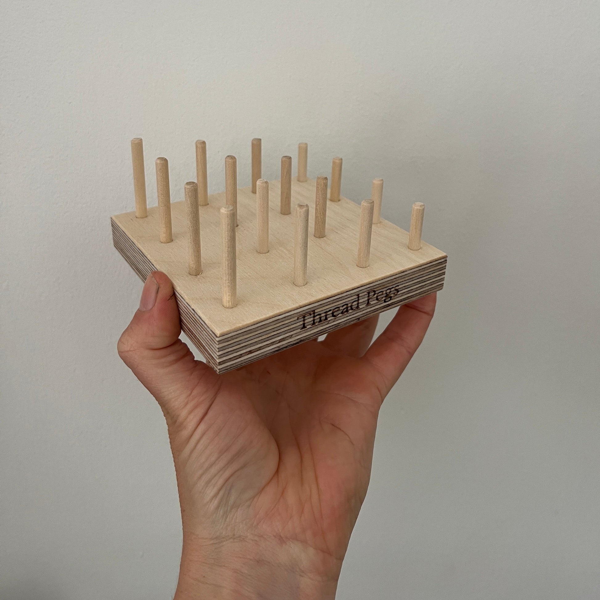 Hand holding a wooden tool with pegs for bobbins against a plain background