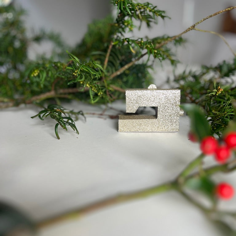 Silver sewing machine ornament on a branch with green leaves and red berries