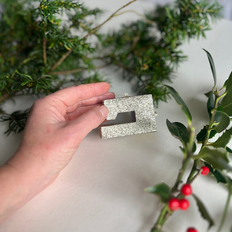 Miniature sewing machine Christmas ornament with hand holding it.
