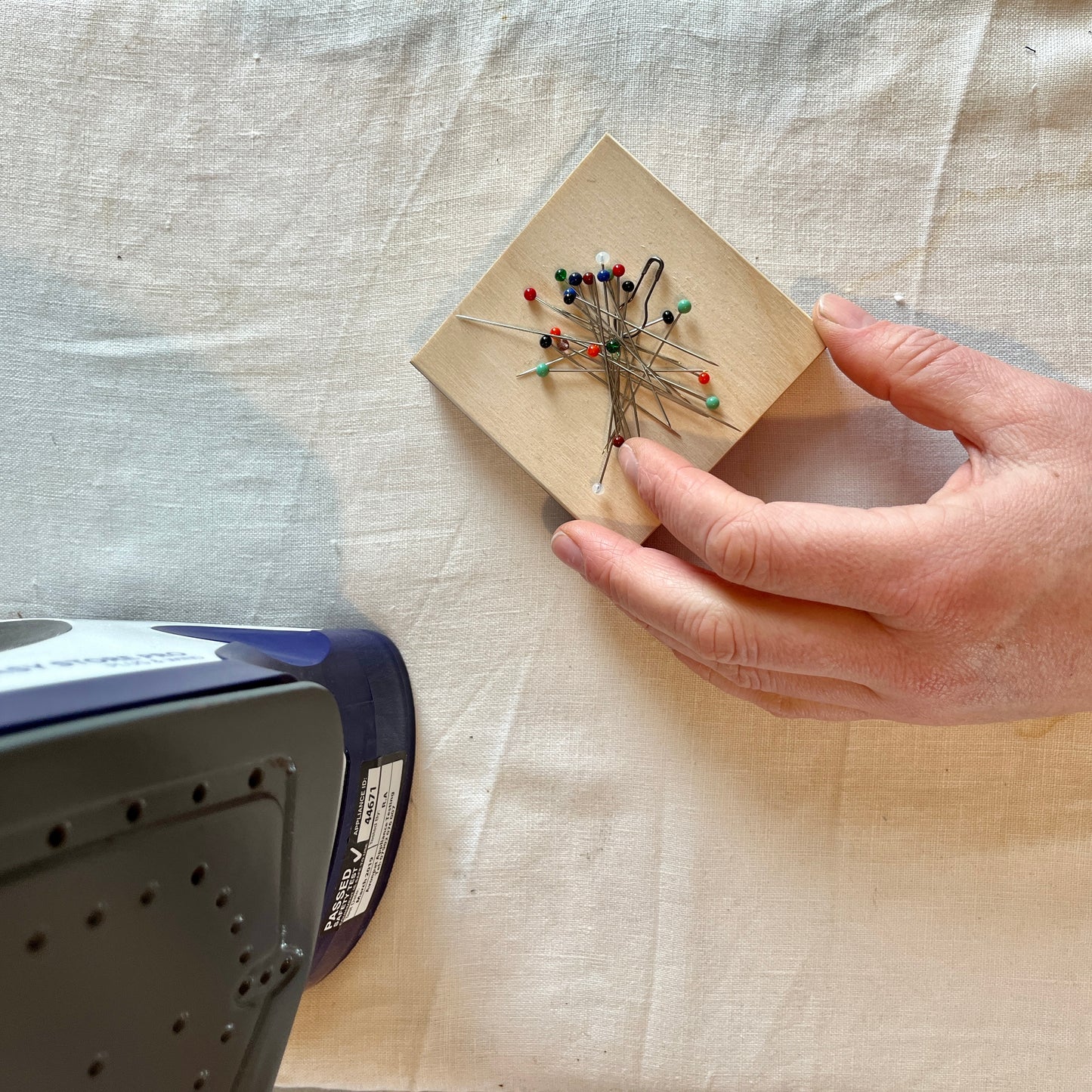 Hand holding a wooden block with pins on a fabric background