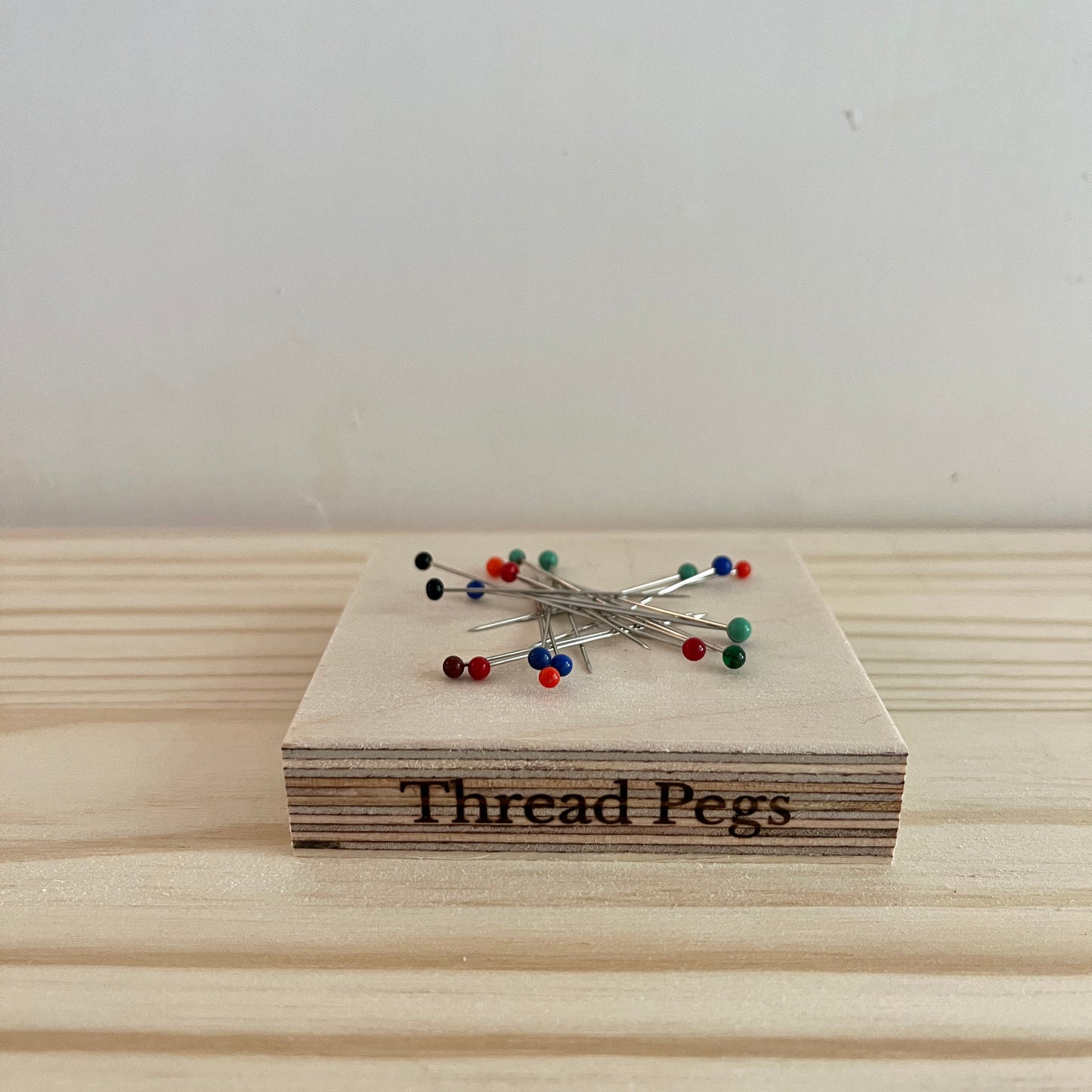 Wooden block with 'Thread Pegs' and pins on a light wooden surface