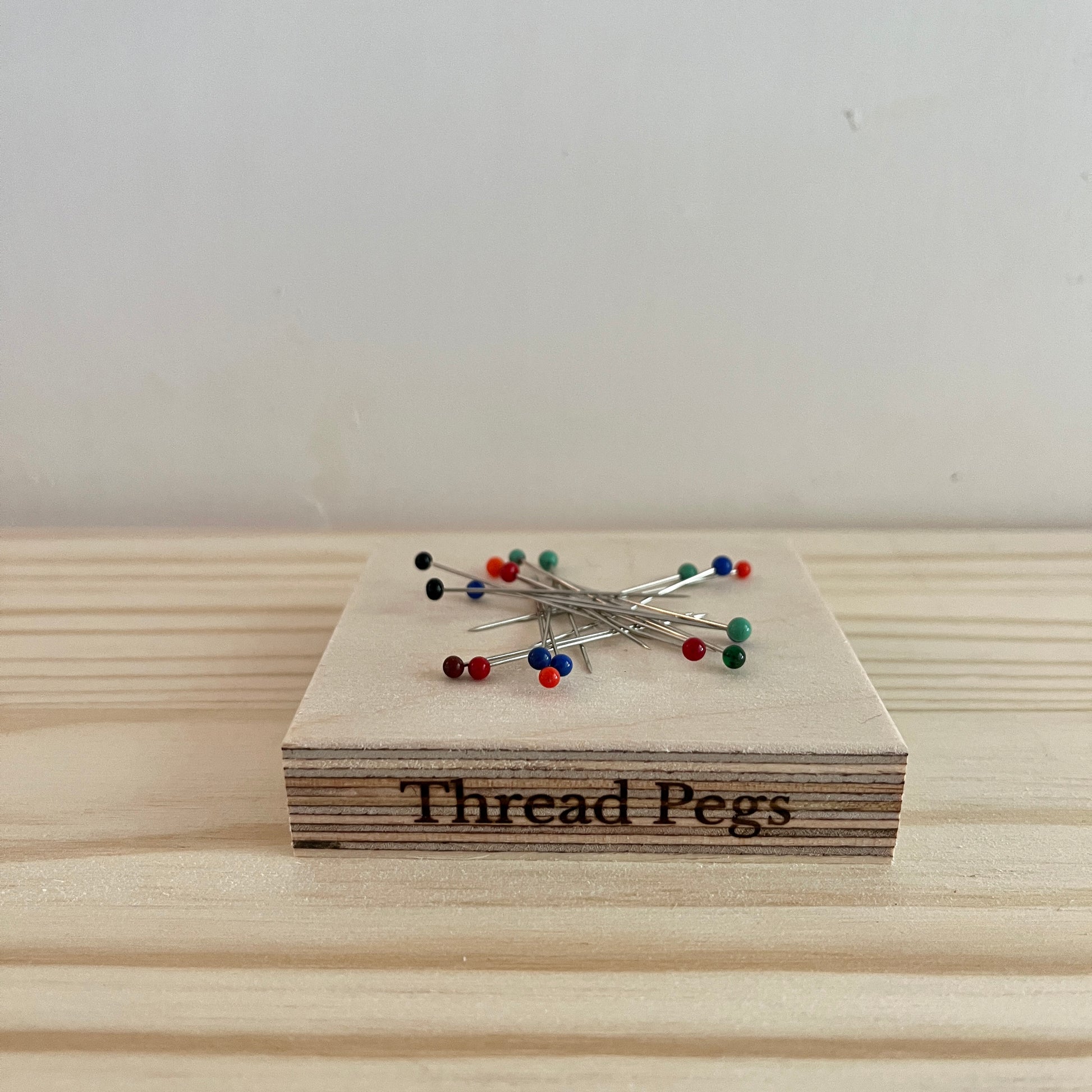 Wooden block with 'Thread Pegs' and pins on a light wooden surface